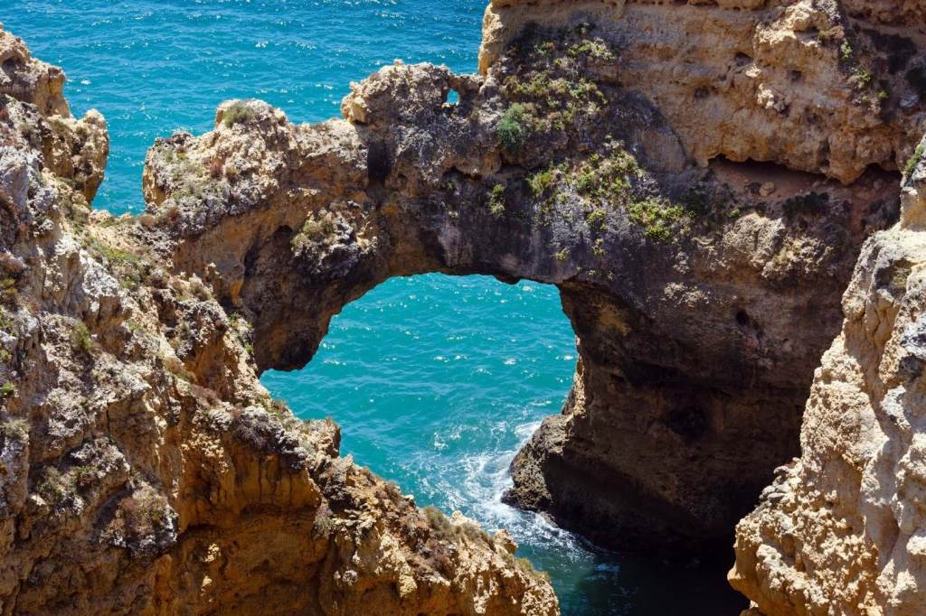 Rock arch over turquoise sea with clear blue sky.