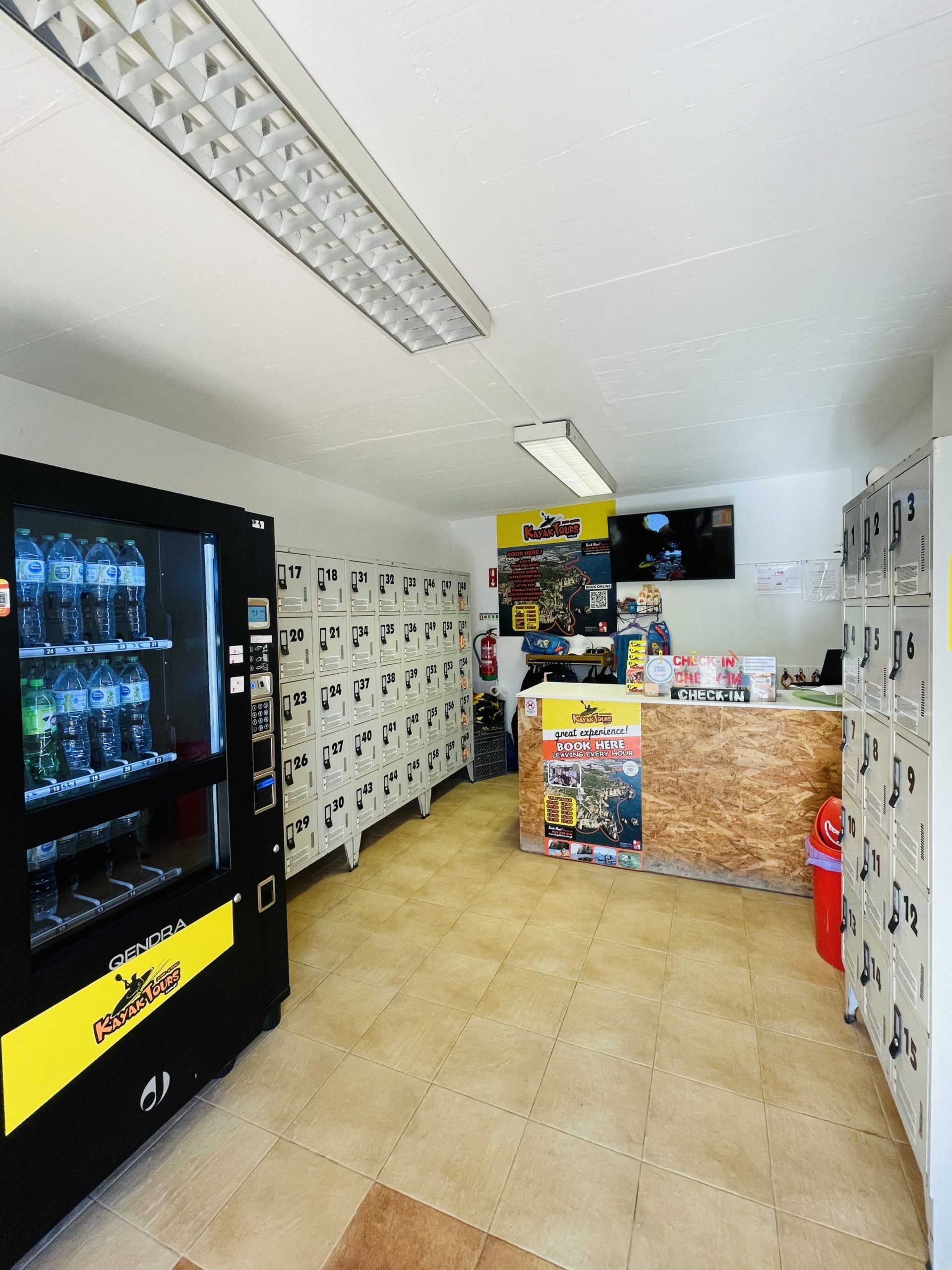 Room with lockers, a vending machine, and a counter with promotional posters.